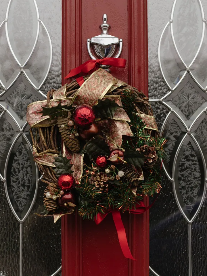 A Christmas wreath with red ornaments and ribbon on a red front door